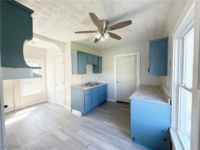 kitchen featuring ceiling fan, a textured ceiling, light countertops, a sink, and light wood-style floors