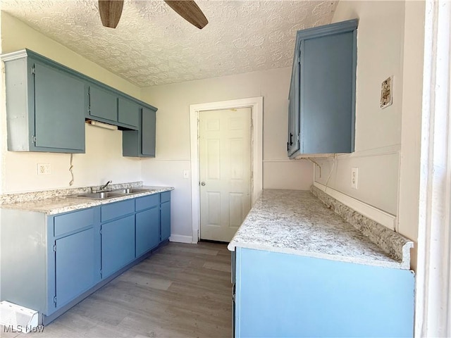 kitchen featuring a sink, light countertops, a textured ceiling, light wood-style flooring, and a ceiling fan