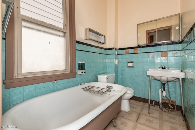 bathroom featuring toilet, tile patterned floors, wainscoting, and a freestanding tub