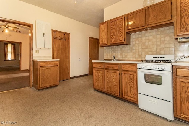 kitchen with light countertops, white range with gas cooktop, brown cabinets, and decorative backsplash