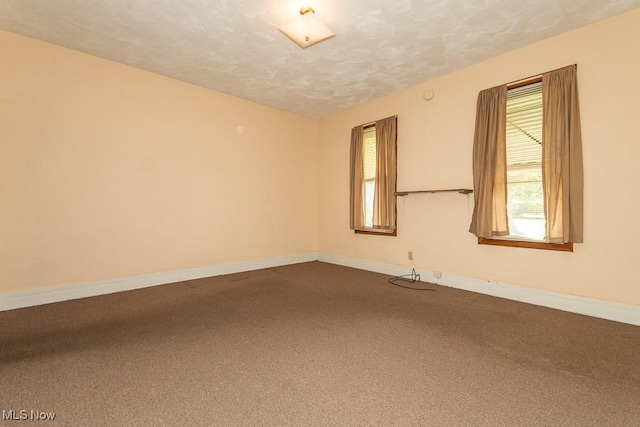 empty room featuring a textured ceiling, baseboards, and dark colored carpet