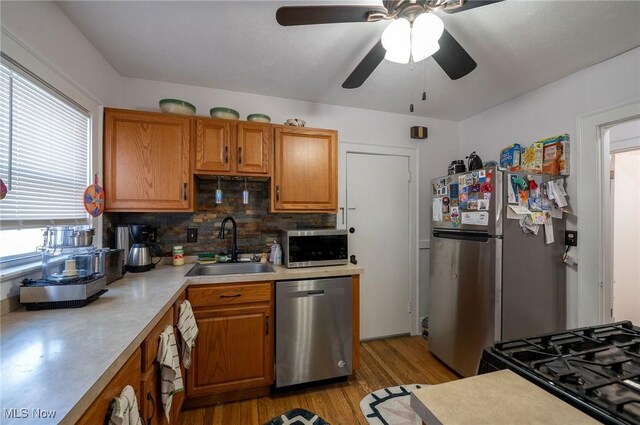 kitchen with appliances with stainless steel finishes, a sink, light wood finished floors, light countertops, and tasteful backsplash