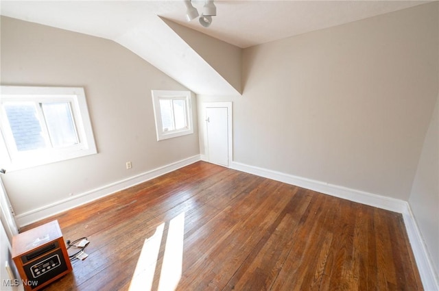additional living space with baseboards, wood-type flooring, and vaulted ceiling