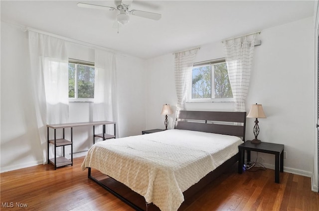 bedroom featuring wood-type flooring, baseboards, ceiling fan, and multiple windows