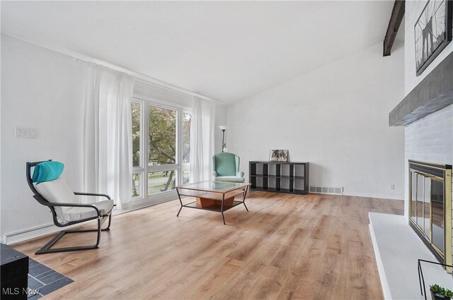 sitting room featuring vaulted ceiling, a glass covered fireplace, wood finished floors, and visible vents