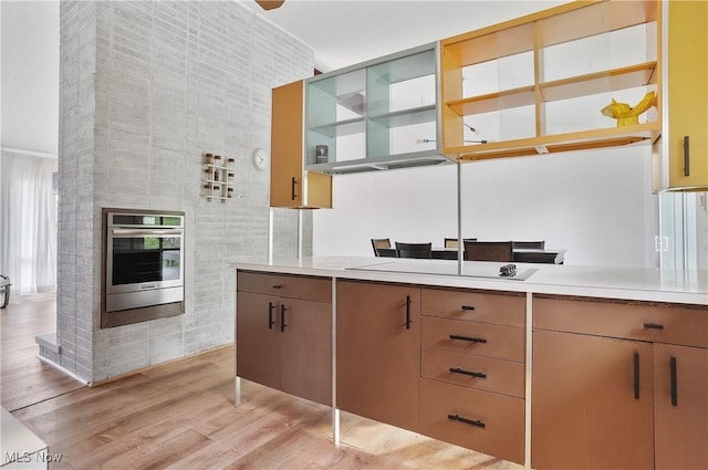 kitchen with light wood-type flooring, open shelves, stainless steel oven, and light countertops