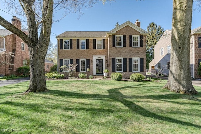 colonial-style house with a chimney, a front lawn, and brick siding