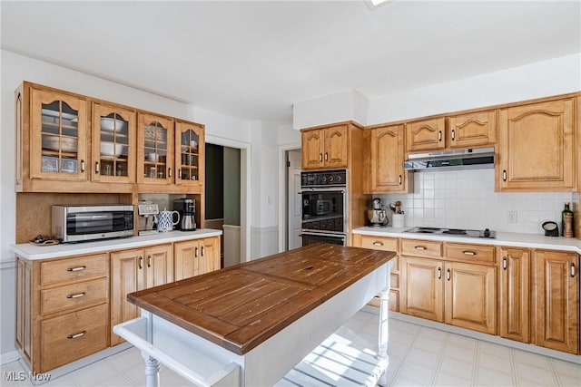 kitchen featuring dobule oven black, glass insert cabinets, electric stovetop, under cabinet range hood, and backsplash