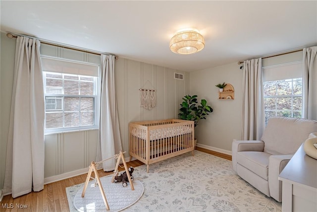 bedroom featuring baseboards, a nursery area, light wood-style flooring, and visible vents