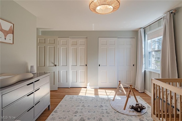 bedroom featuring baseboards, light wood-style flooring, and two closets