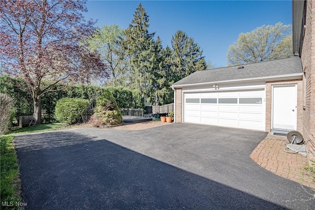 view of side of home featuring brick siding, a garage, roof with shingles, and driveway