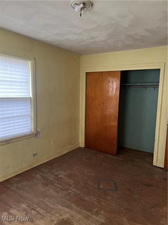 unfurnished bedroom featuring a closet, baseboards, and dark wood-style floors