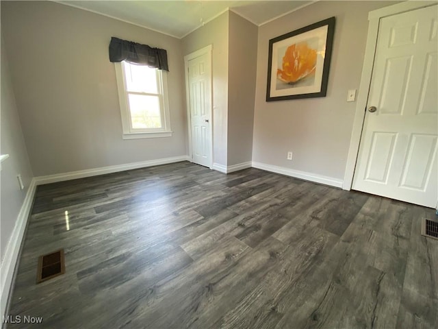 unfurnished bedroom featuring visible vents, ornamental molding, dark wood finished floors, and baseboards