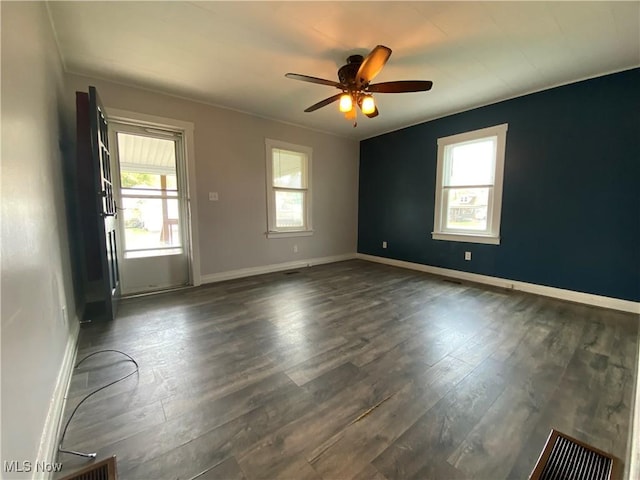 empty room featuring dark wood-type flooring, a ceiling fan, and baseboards