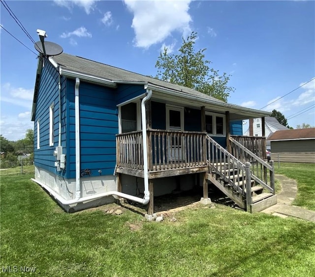 back of house with a lawn, covered porch, roof with shingles, and stairs