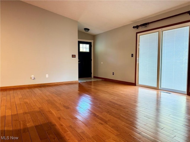 unfurnished room with light wood-style floors, baseboards, vaulted ceiling, and visible vents