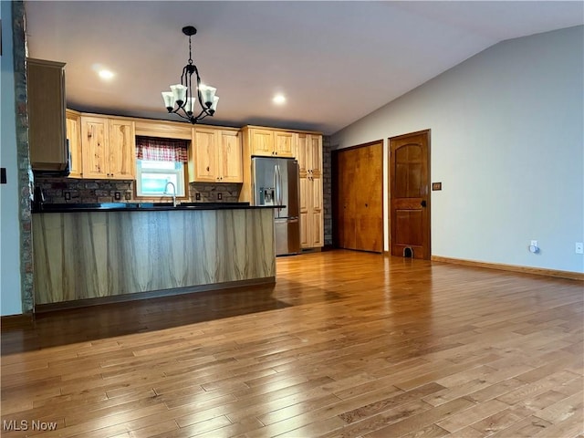 kitchen with an inviting chandelier, dark countertops, a peninsula, lofted ceiling, and stainless steel fridge