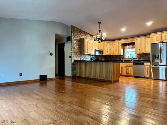 kitchen with dark countertops, a notable chandelier, a sink, stainless steel appliances, and vaulted ceiling