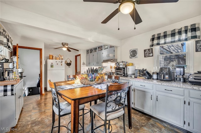 kitchen with freestanding refrigerator, gray cabinets, a ceiling fan, and under cabinet range hood