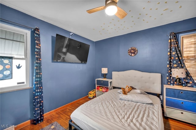bedroom featuring a ceiling fan, baseboards, multiple windows, and wood finished floors