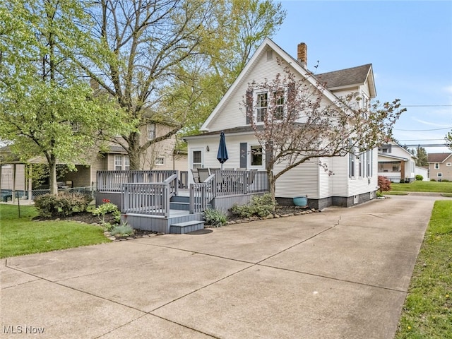 view of front of house with a shingled roof, a wooden deck, driveway, and a chimney