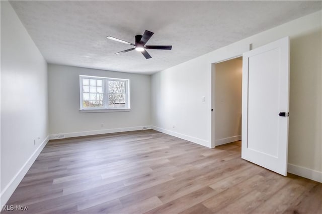 empty room with baseboards, a ceiling fan, and light wood finished floors