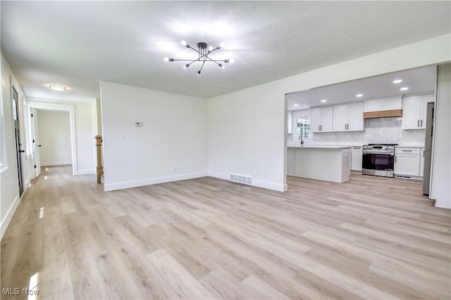 unfurnished living room featuring visible vents, light wood-style flooring, baseboards, and a notable chandelier