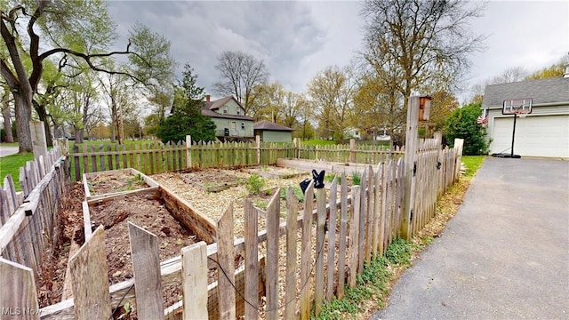 view of yard featuring a garage, fence, driveway, and a vegetable garden