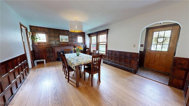dining room with wooden walls, arched walkways, light wood finished floors, and a wainscoted wall