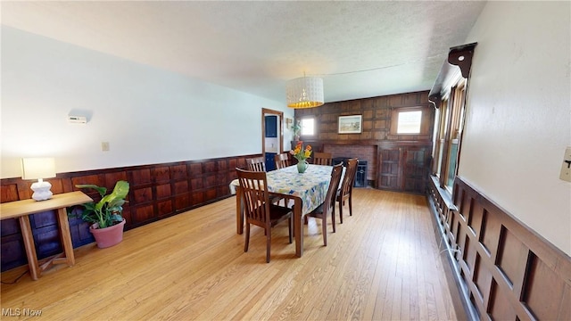 dining room featuring a notable chandelier, wood walls, wainscoting, and light wood-type flooring
