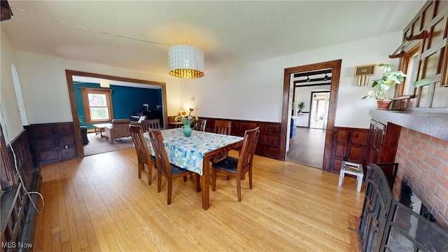 dining space featuring light wood-style floors, a wainscoted wall, a brick fireplace, and wood walls