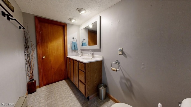 bathroom with a textured ceiling, tile patterned floors, baseboards, vanity, and toilet
