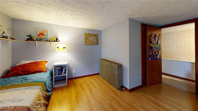 bedroom featuring wood finished floors, baseboards, a textured ceiling, and radiator heating unit