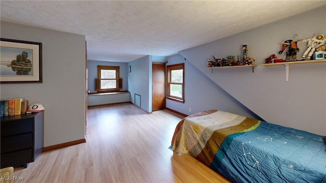 bedroom with light wood-style floors, a textured ceiling, and baseboards