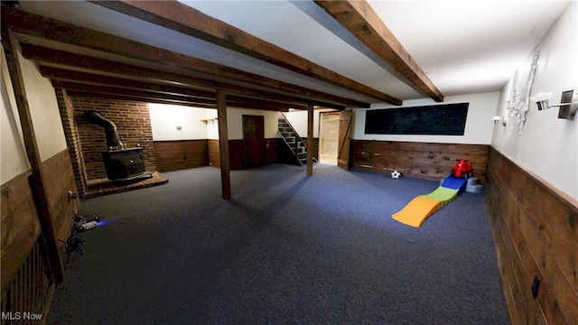 recreation room featuring carpet floors, a wood stove, a wainscoted wall, and wood walls
