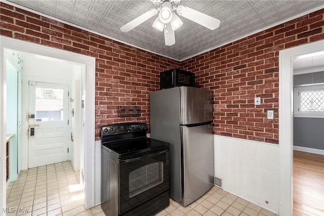 kitchen featuring black electric range, freestanding refrigerator, and brick wall