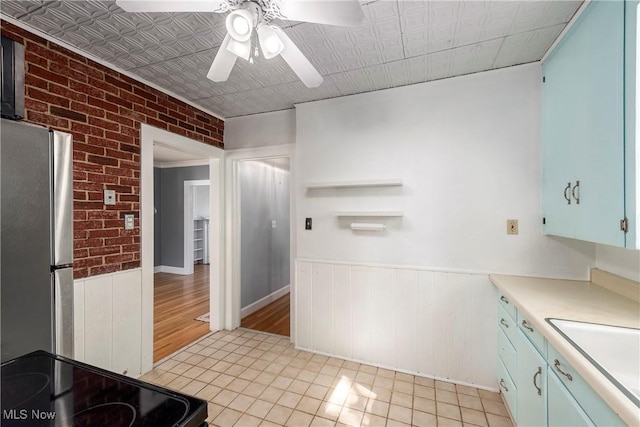kitchen with ceiling fan, wainscoting, light countertops, freestanding refrigerator, and light tile patterned floors