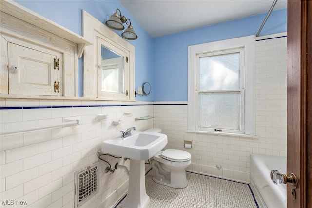 full bath featuring toilet, tile patterned floors, tile walls, a tub to relax in, and visible vents
