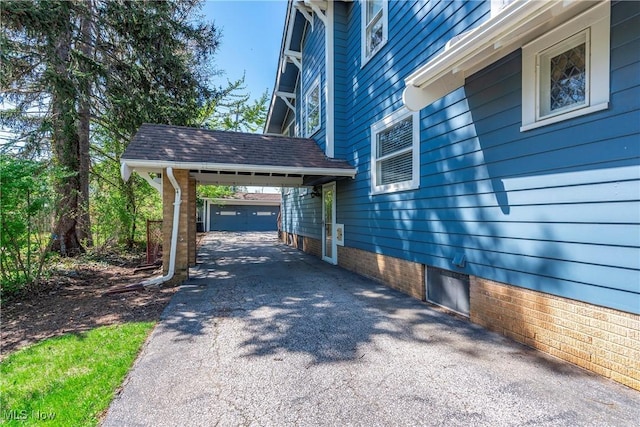 view of property exterior featuring an outdoor structure, a carport, and aphalt driveway