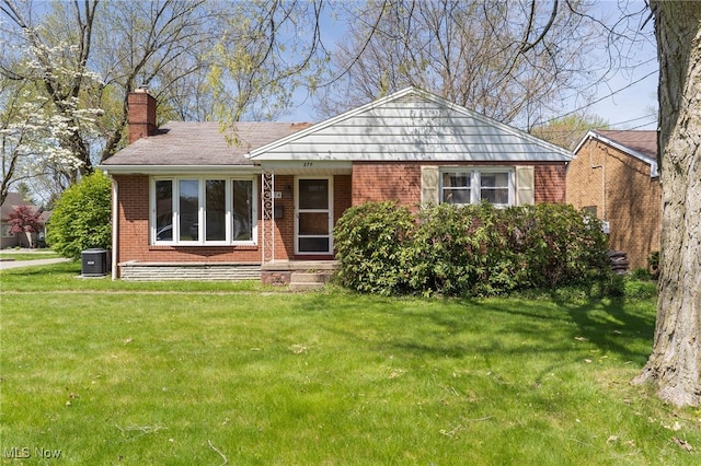 view of front of house with brick siding, a front lawn, a chimney, and cooling unit