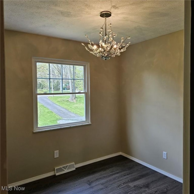 spare room with an inviting chandelier, a textured ceiling, baseboards, visible vents, and dark wood-style floors