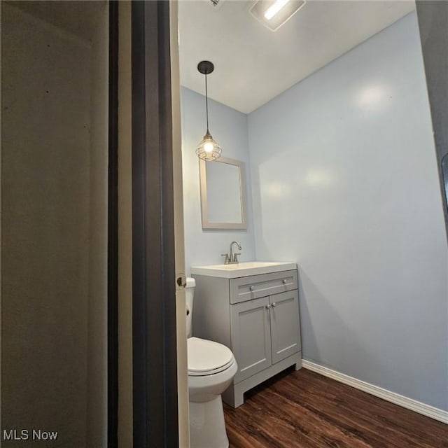 half bath with vanity, baseboards, wood finished floors, and toilet