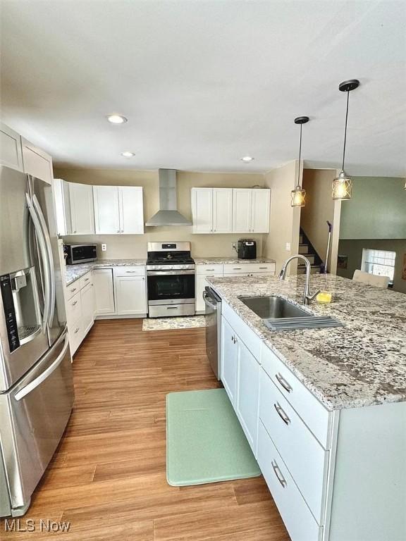 kitchen featuring a sink, appliances with stainless steel finishes, wall chimney exhaust hood, and white cabinetry