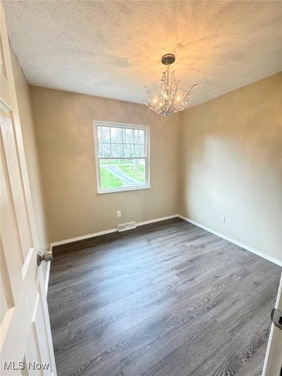 2939 Lindale Dr, Akron, OH 44312 - spare room with dark wood-style flooring, a textured ceiling, an inviting chandelier, and visible vents