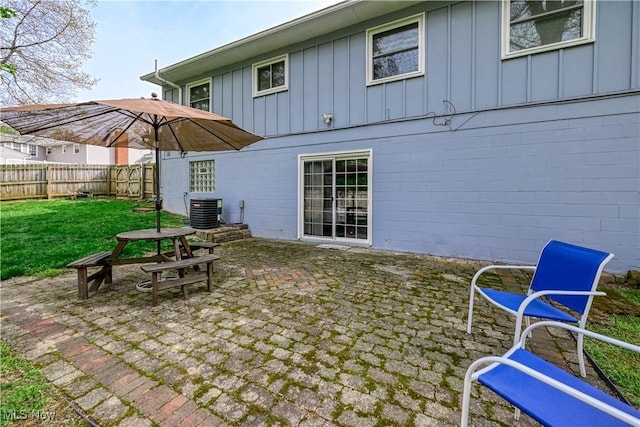 rear view of property featuring cooling unit, a fenced backyard, board and batten siding, a patio area, and a lawn