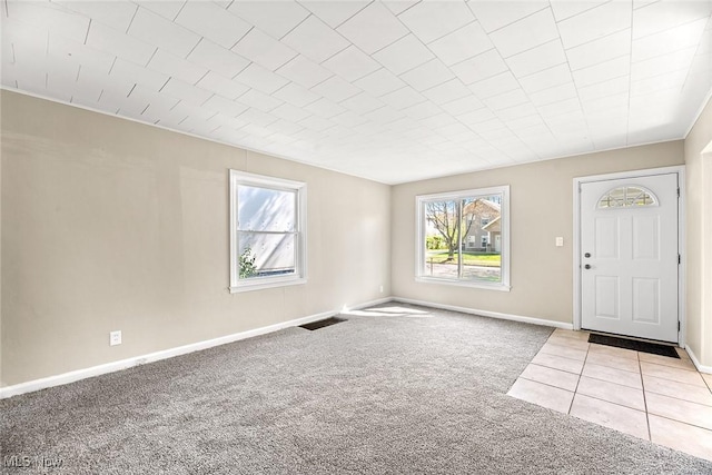 foyer featuring baseboards, a wealth of natural light, visible vents, and light colored carpet