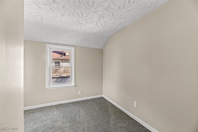 carpeted spare room featuring a textured ceiling, vaulted ceiling, and baseboards