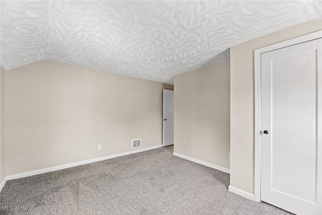 carpeted empty room with baseboards, visible vents, and lofted ceiling