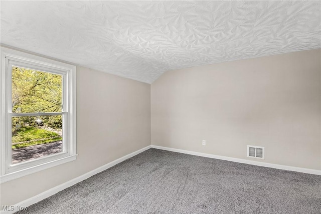carpeted spare room featuring visible vents, a textured ceiling, baseboards, and vaulted ceiling