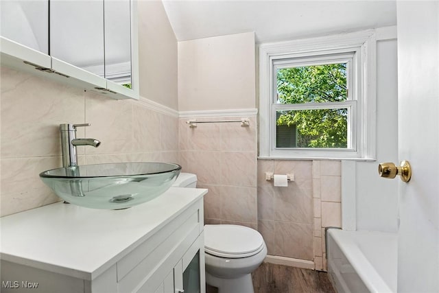 full bathroom featuring vanity, toilet, a tub, tile walls, and wood finished floors